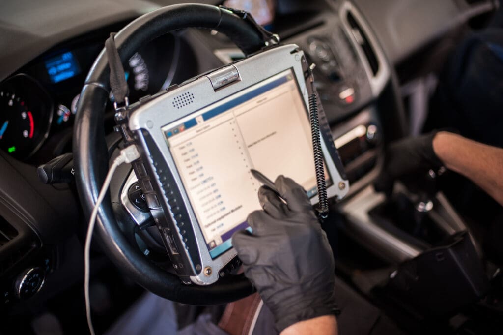 Automobile computer diagnosis. Car mechanic repairer looks for engine failure on diagnostics equipment in vehicle service workshop