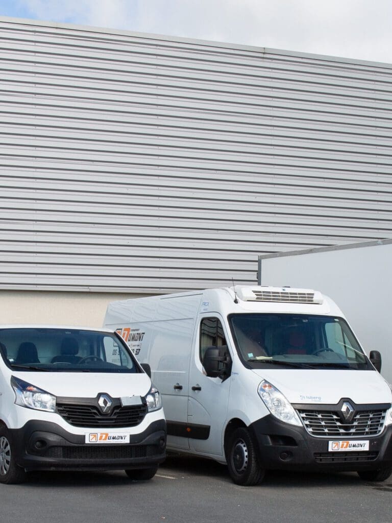 Two white Renault vans, marked with company logos, are parked side by side in front of a modern industrial building. The setting showcases an Approved Garage specializing in MOT Servicing and Car Servicing.